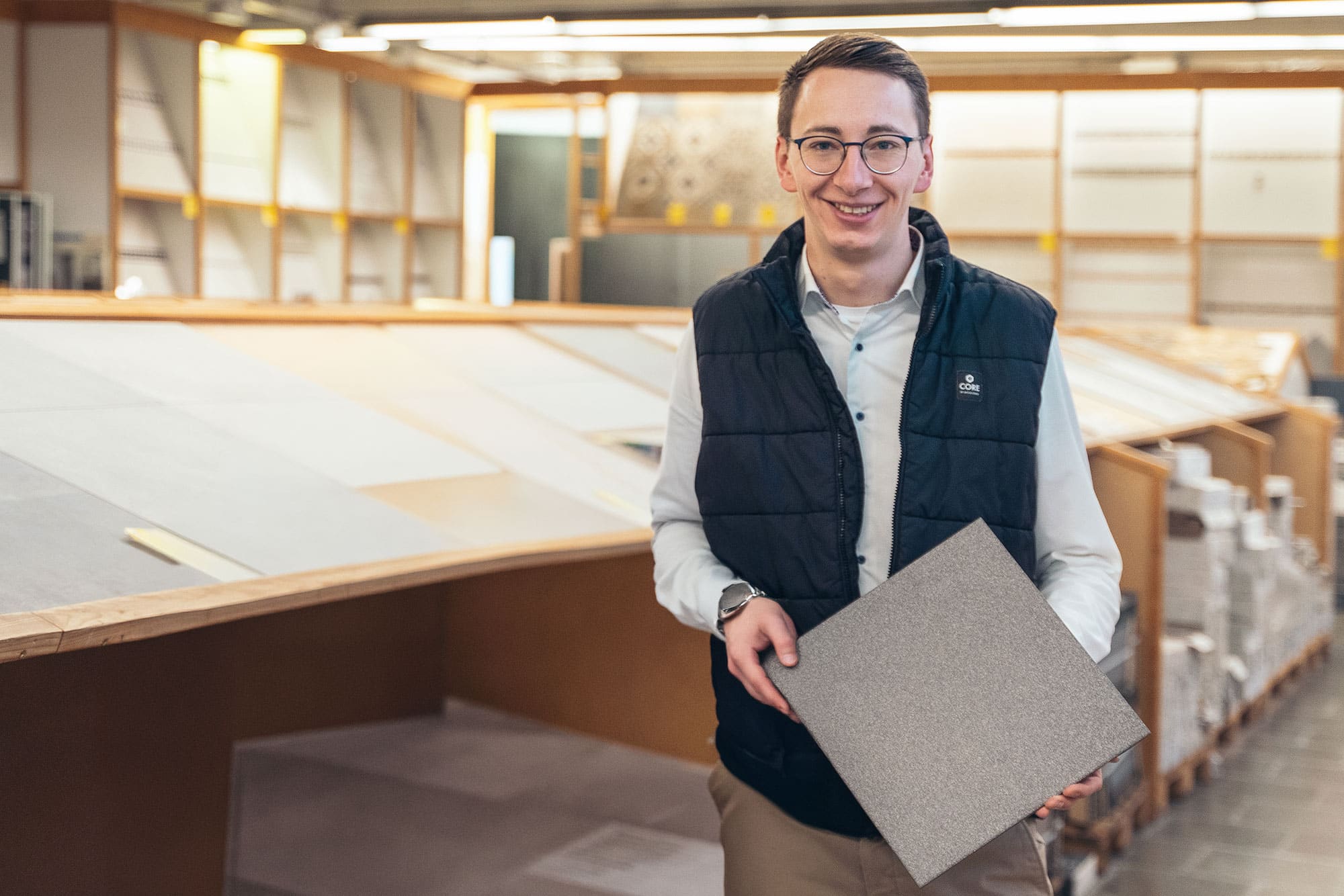 Die Geschäftsführer Matthias Lanzl und Lucas Eigen vom Fliesenmarkt-Süd zeigen Fliesen aus ihrem umfangreichen Sortiment. Matthias Lanzl hält eine großformatige, graue Fliese, während Lucas Eigen eine kleinere, ebenfalls graue Fliese präsentiert. Im Hintergrund ist der Ausstellungsbereich mit weiteren Fliesenmustern zu sehen, der die Vielfalt und Qualität des Angebots unterstreicht.